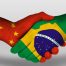 Aperto de mãos entre uma mão pintada com a bandeira da China e a outra do Brasil.